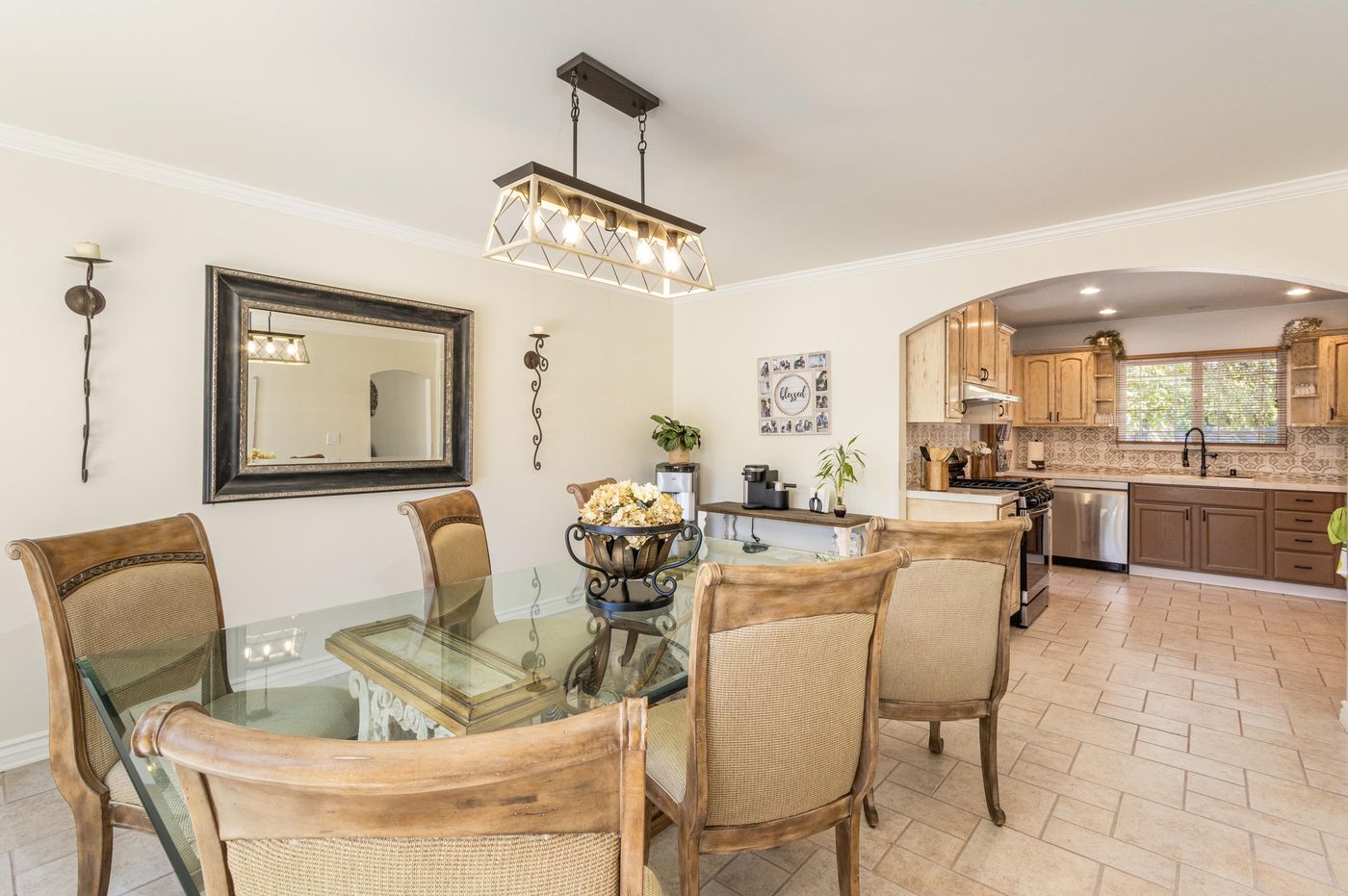 The dining room: a large glass table with upholstered chairs under a pendant light, with the kitchen beyond