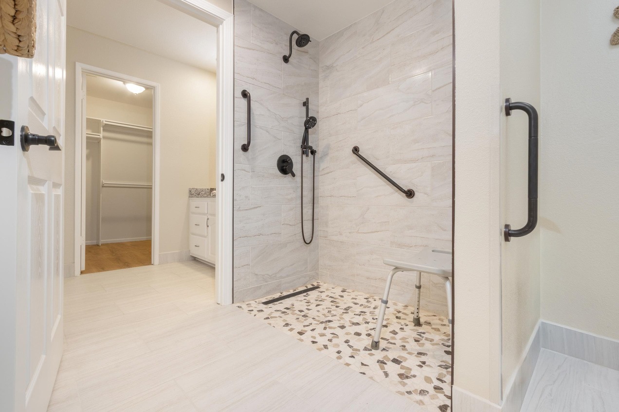 A walk-in shower with no step, grab bars and a shower chair